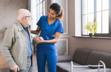 A nurse assisting a senior man by holding his hands and guiding his steps.