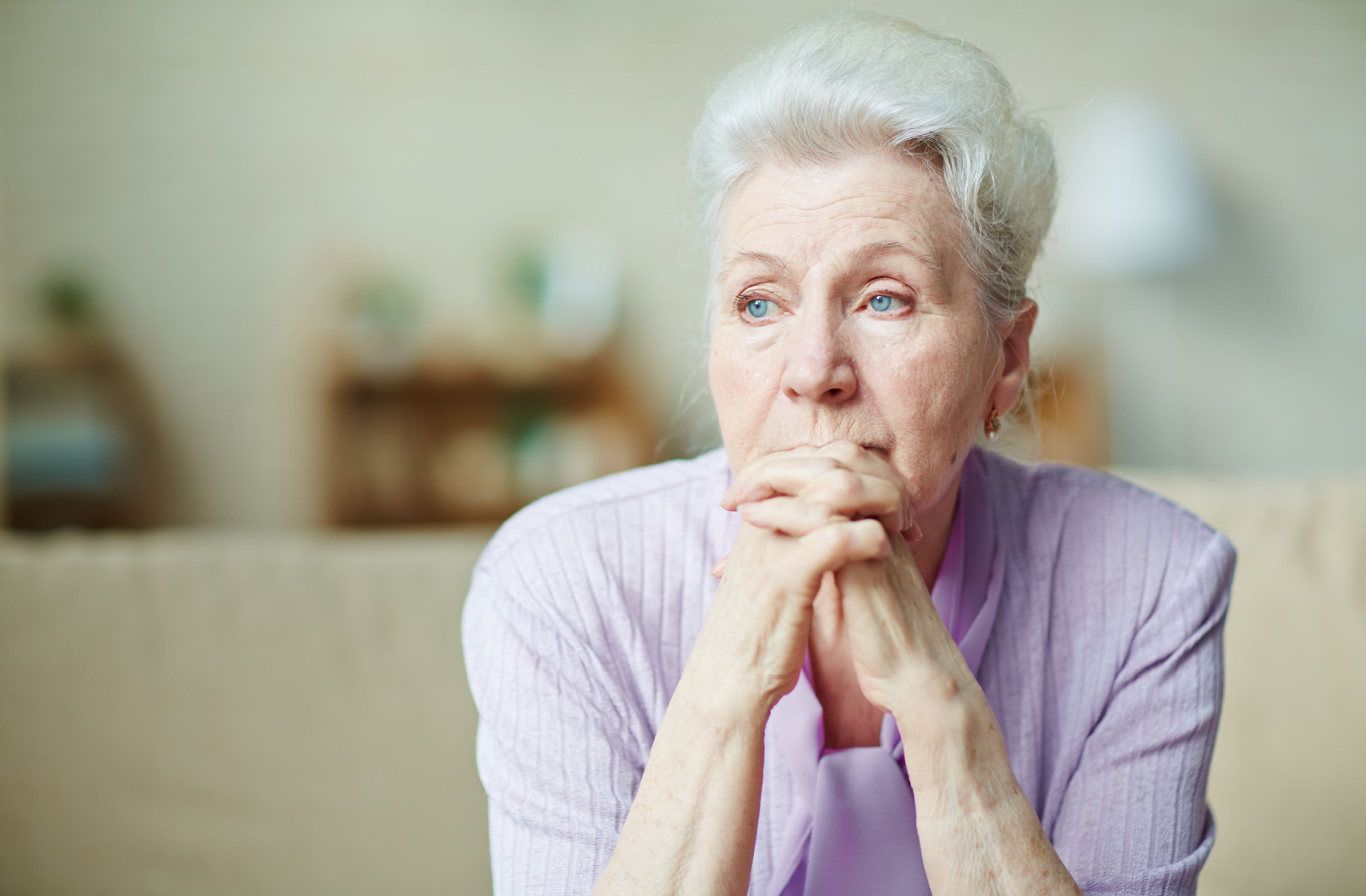 A senior woman with her hand clasped in front of her face.