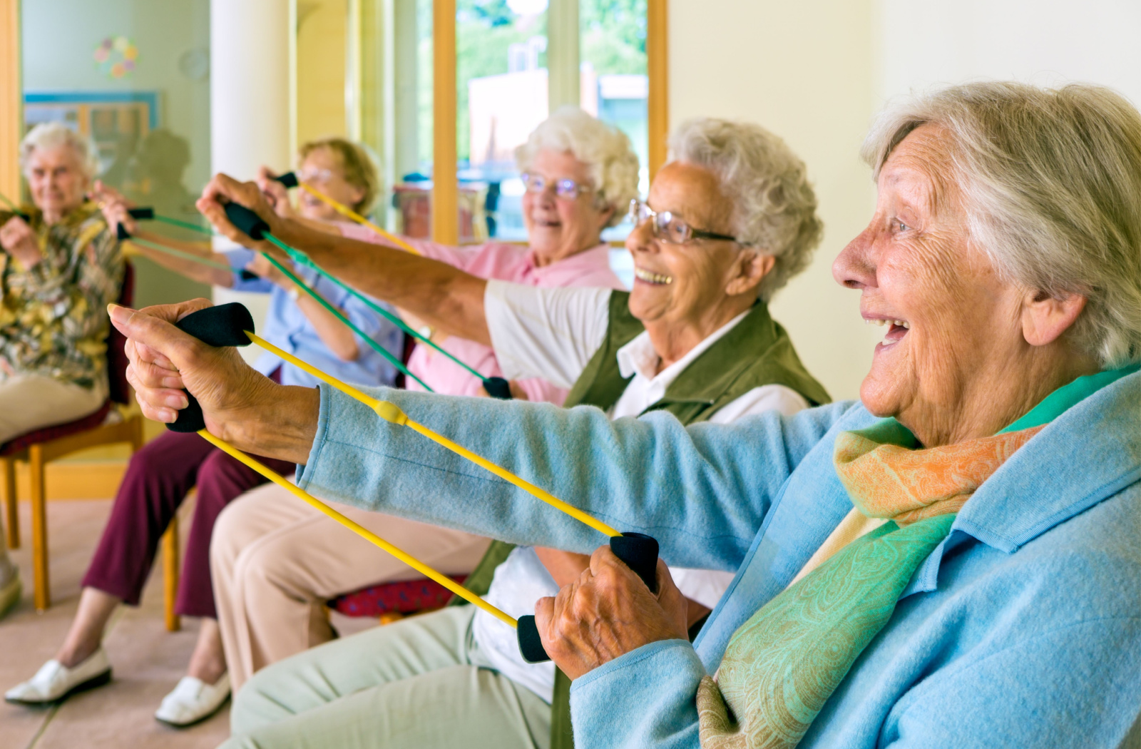 A group of senior women smiling, sitting and exercising together in the living room