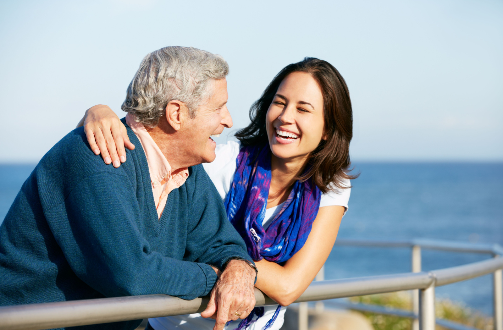 A senior man and his daughter smiling and talking to each other near a beach.