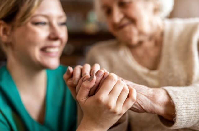 A close up of a nurse holding hands with an older woman