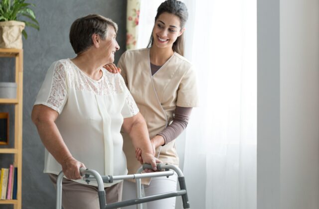 A caregiver in hospice care helping a senior woman with her walker while they smile at each other.