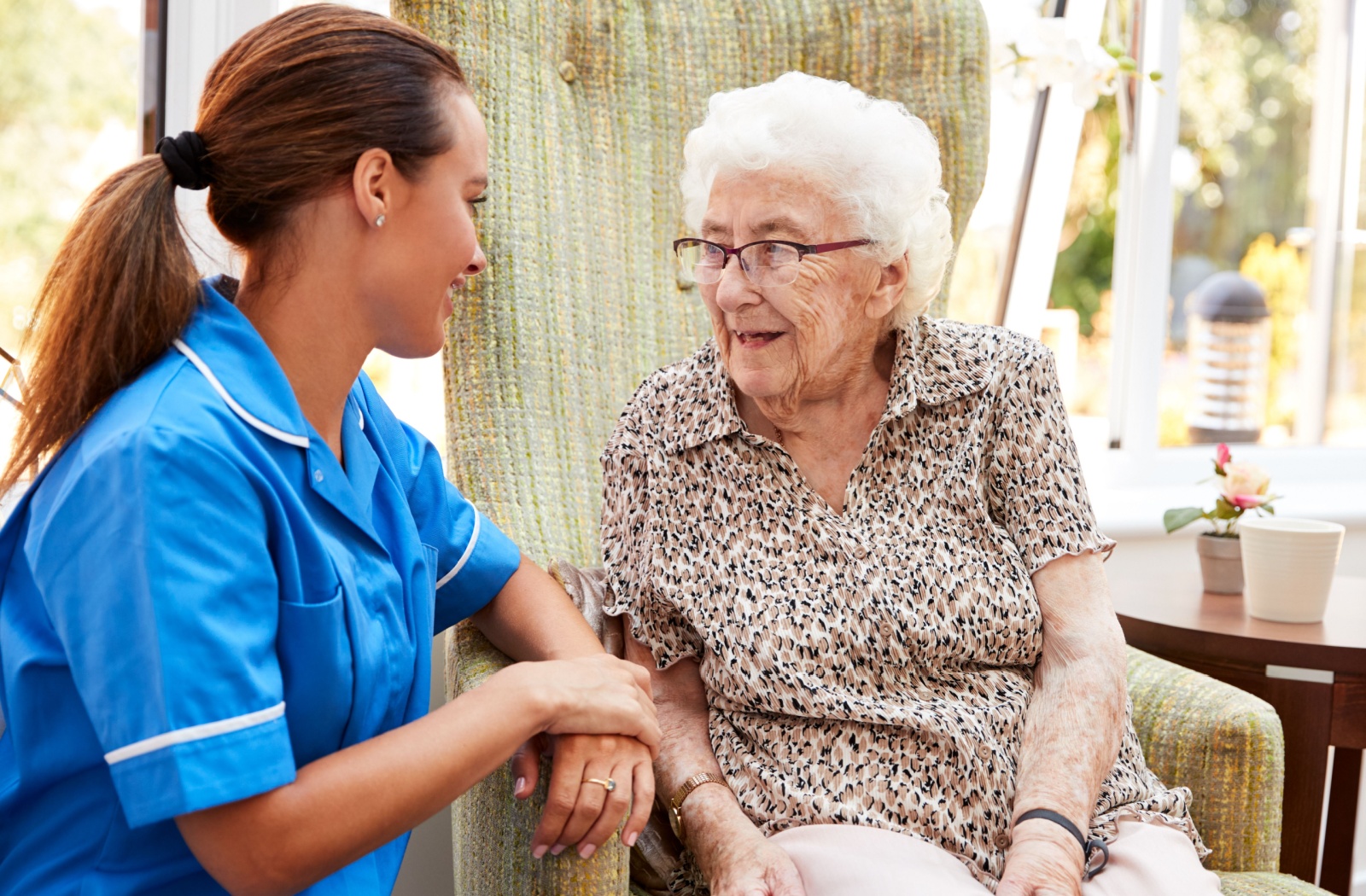 A senior woman in a large chair smiling at a caregiver in hospice care.
