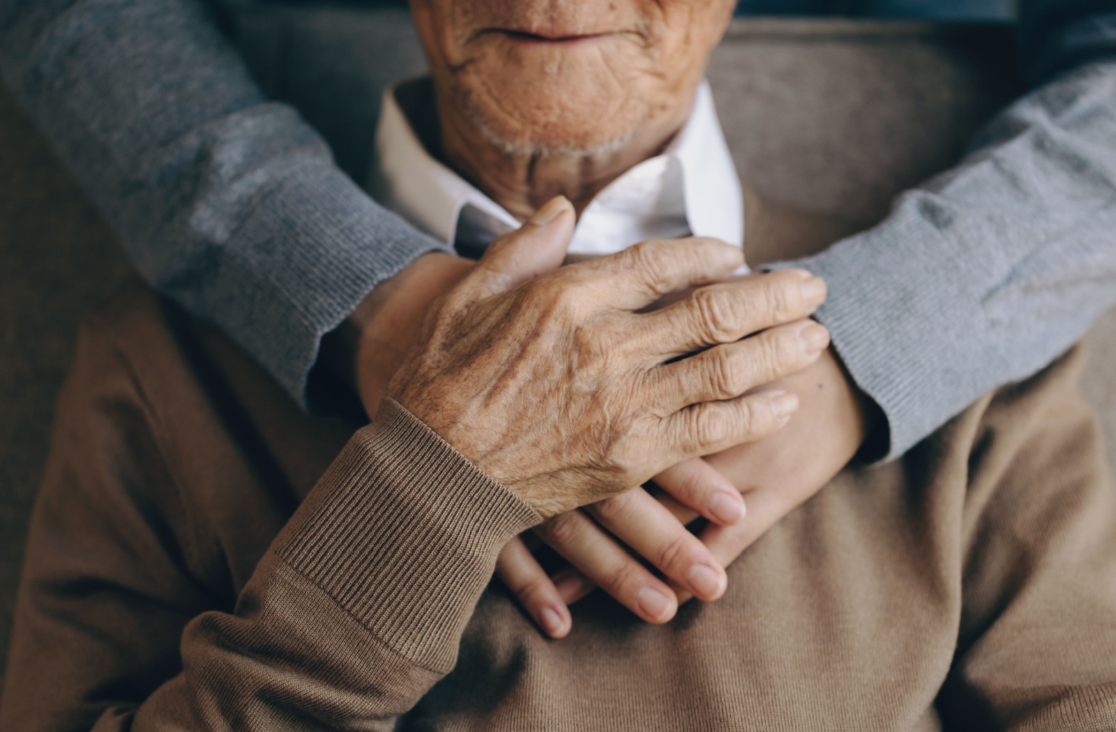 A close up of an elderly man placing his hand overtop of a young woman's hands upon his heart.
