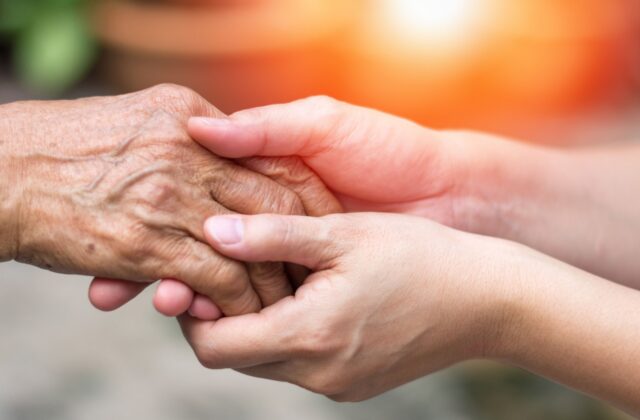 A set of youthful hands embracing an older adult's hand.