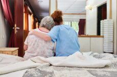 A hospice care home nurse gives a comforting side hug to their ALS patient.