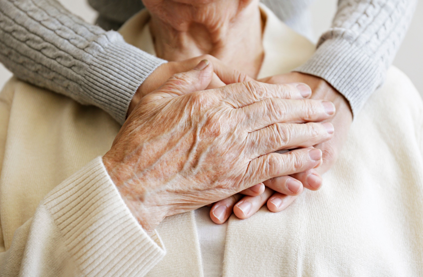 An older adult clasps their hand over a pair of young hands wrapped around them.